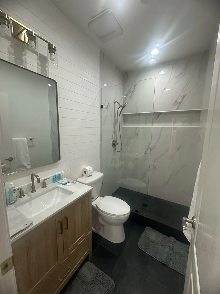 Wood-vanity bathroom with black floor and marble-look shower